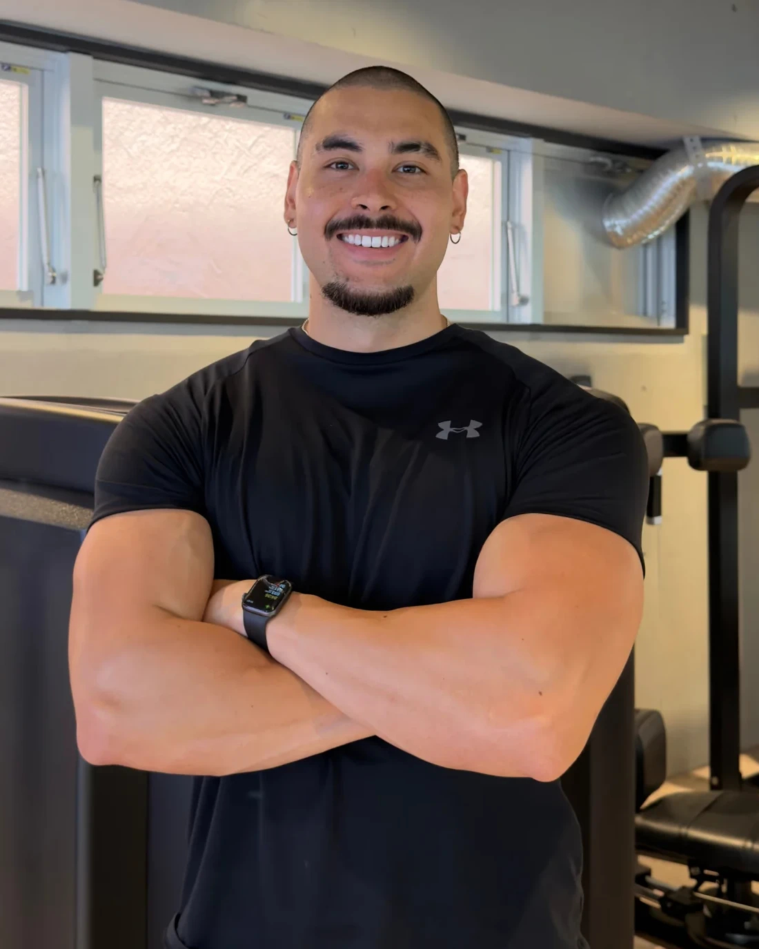 Brendan in a black t-shirt, arms crossed, smiling in a gym