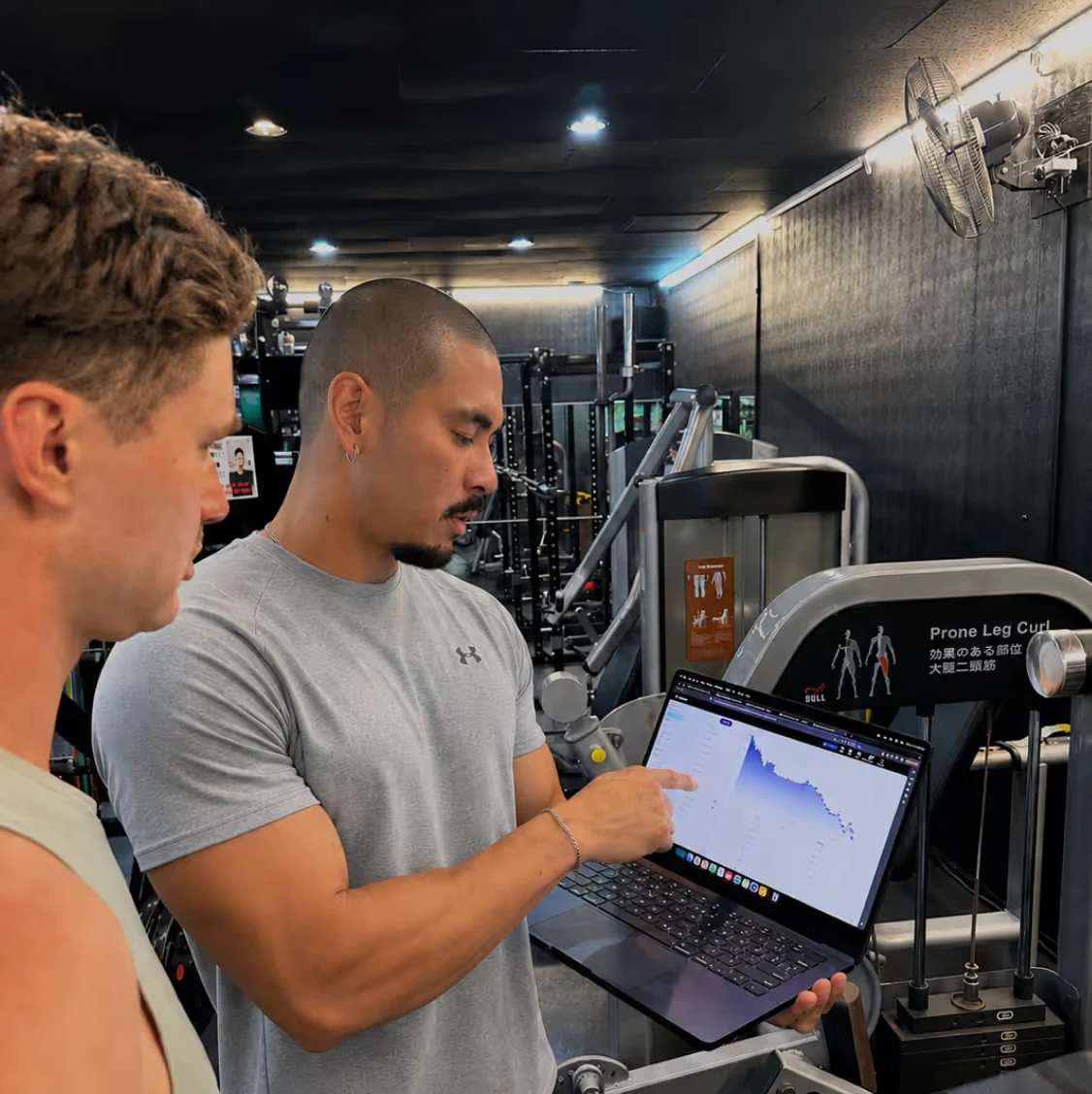 Brendan showing a client a progress chart on a laptop between sets